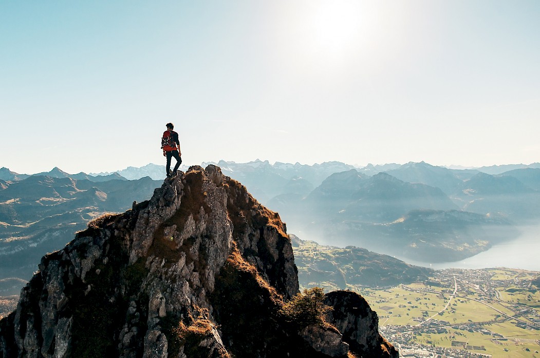 Ein junger Mann steht auf einem Berggipfel und schaut in die Berglandschaft