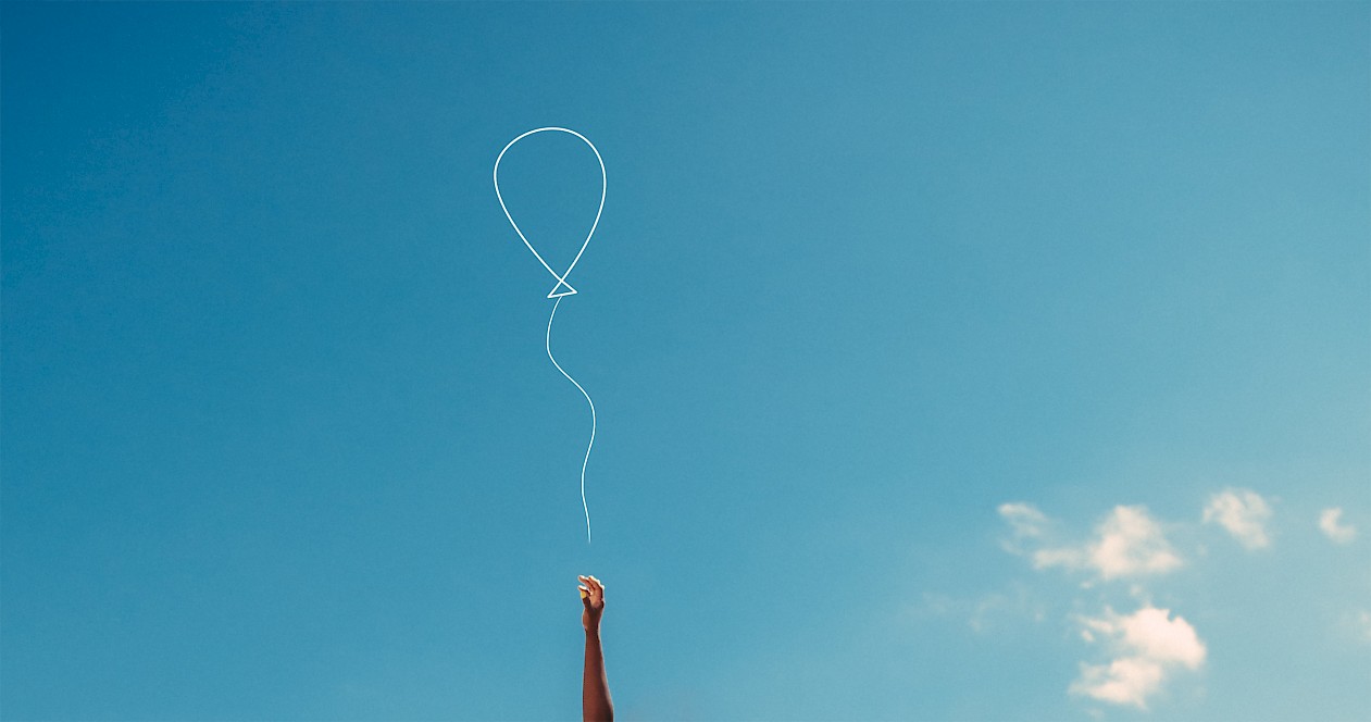 Eine Hand vor einem blauen Himmel lässt einen Luftballon fliegen