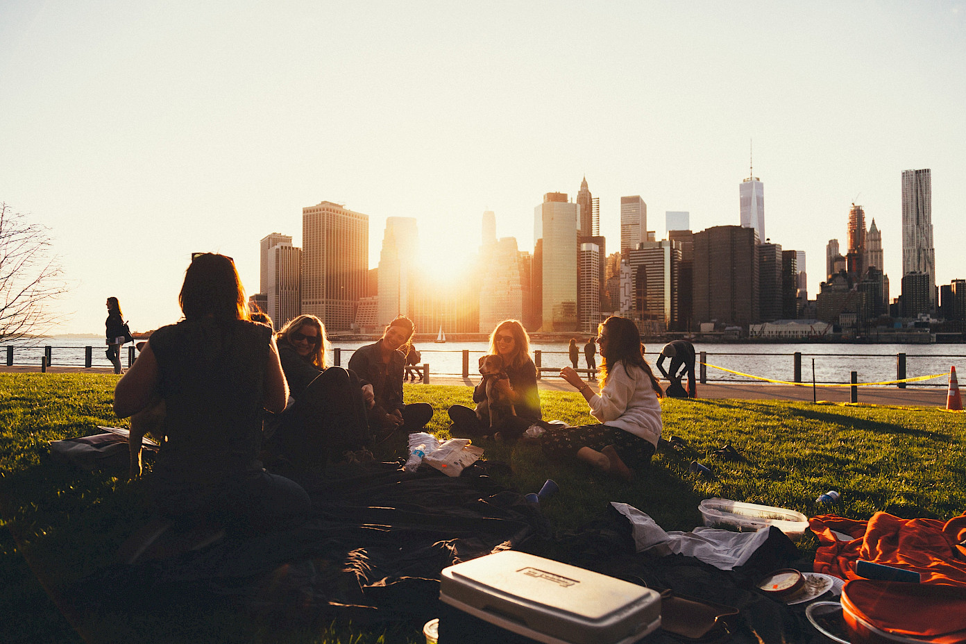 Eine Gruppe junger Leute sitzt zusammen bei Sonnenuntergang auf einer Wiese mit einer Skyline im Hintergrund