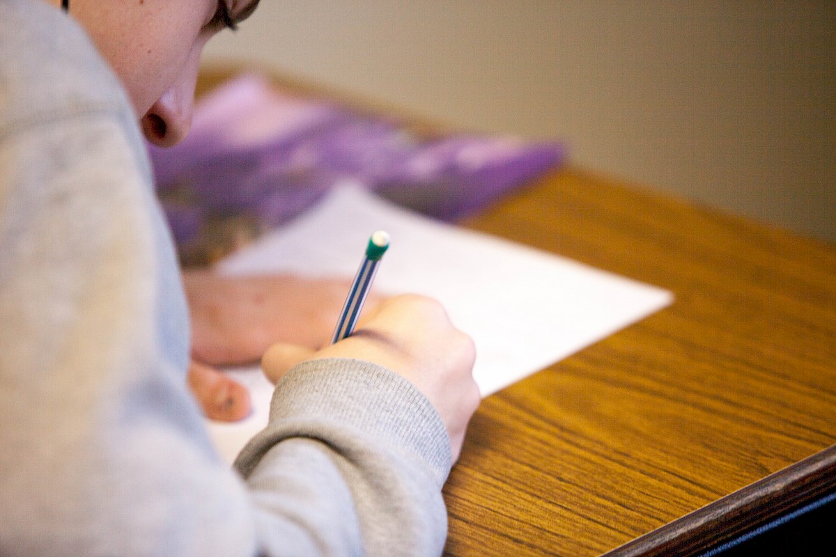 Ein Schüler sitzt am Tisch und schreibt etwas auf ein Blatt Papier