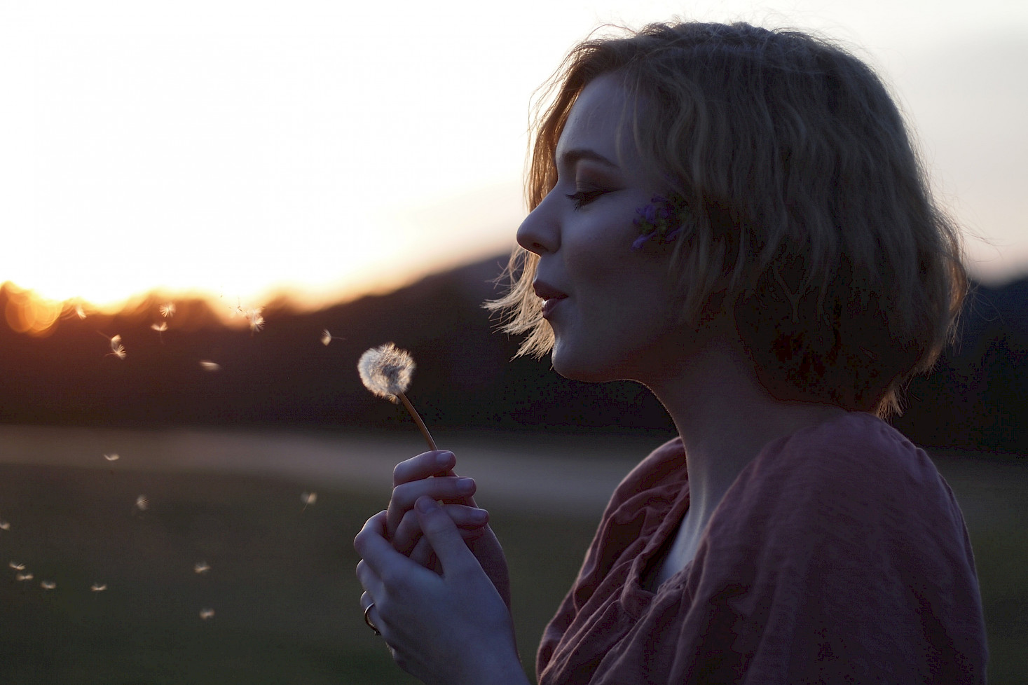 Ein Mädchen hat eine Pusteblume in der Hand und pustet sie an