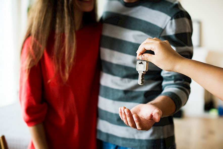 Ein Pärchen steht nebeneinander und jemand hält ihnen einen Wohnungsschlüssel hin