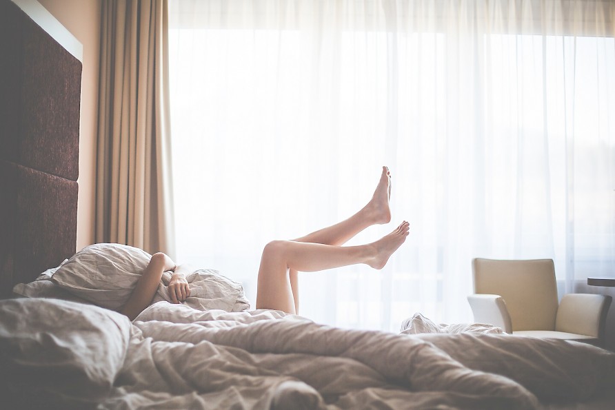 Frau liegt im Bett und strampelt mit ihren Beinen
