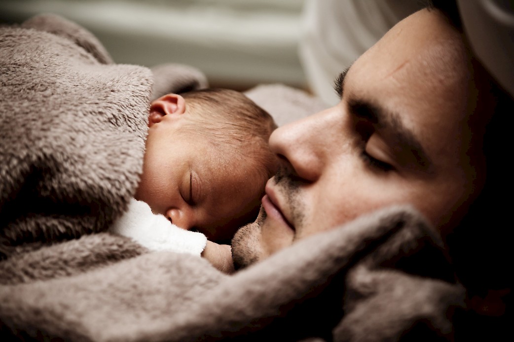 Ein Mann liegt mit einem Baby im Arm im Bett
