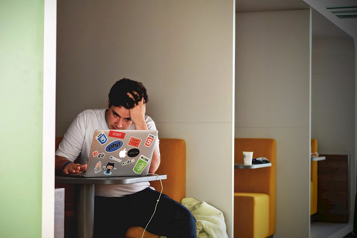 Ein Mann sitzt an einem Tisch vor seinem Laptop und stützt seinen Kopf auf seine Hand