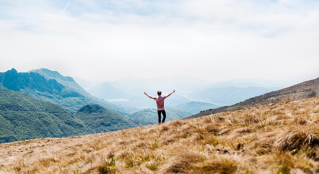Jugendlicher in einer Berglandschaft breitet Arme aus