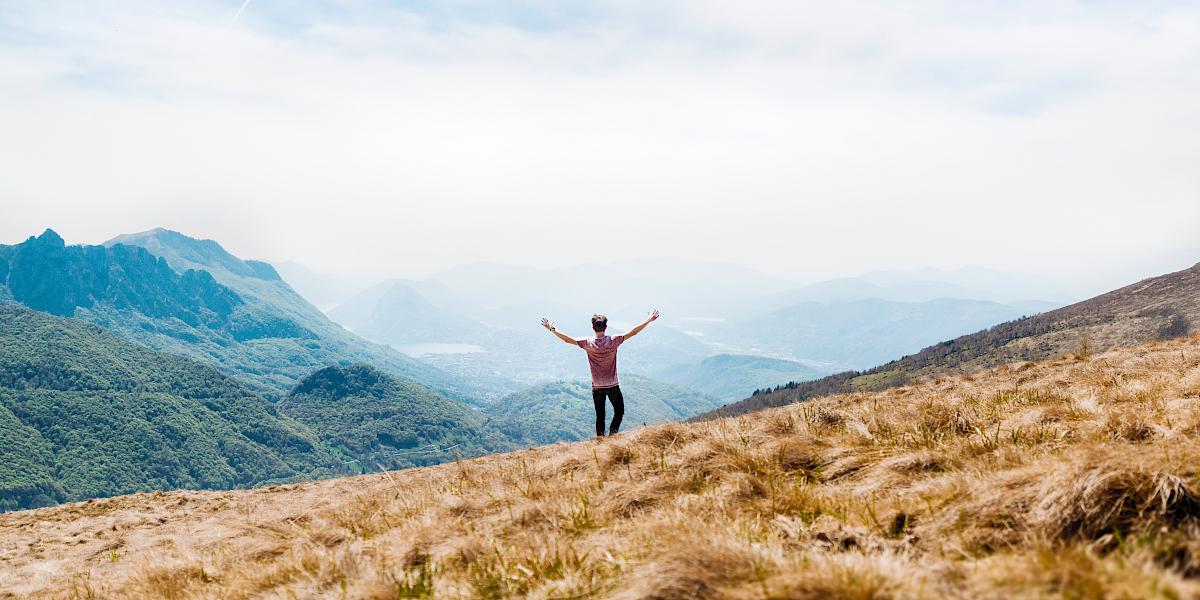 Jugendlicher in einer Berglandschaft breitet Arme aus