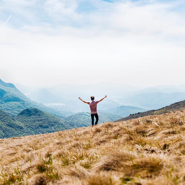 Jugendlicher in einer Berglandschaft breitet Arme aus