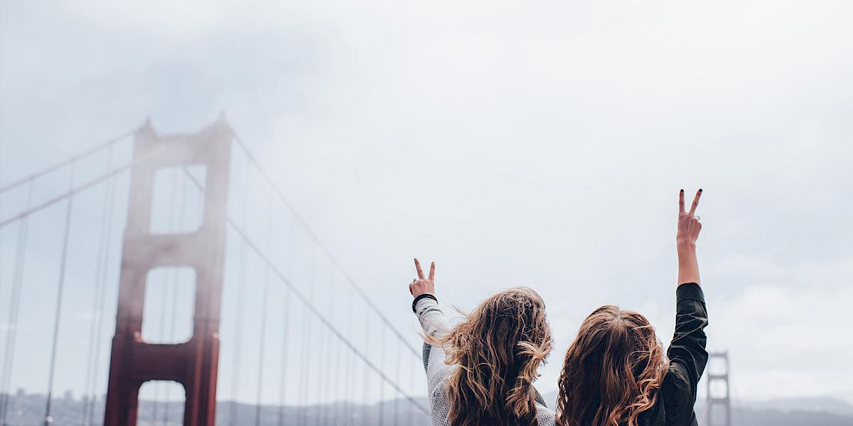 Zwei Frauen an der Golden Gate Bridge strecken die Arme in die Luft