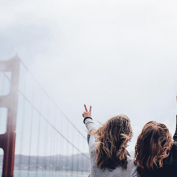 Zwei Frauen an der Golden Gate Bridge strecken die Arme in die Luft