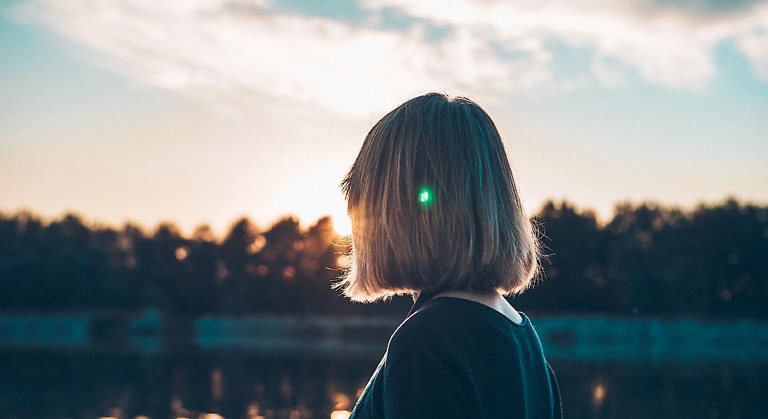 Frau an einem See blickt der Sonne entgegen