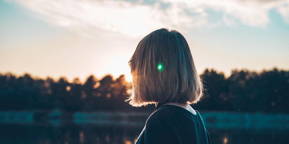 Frau an einem See blickt der Sonne entgegen