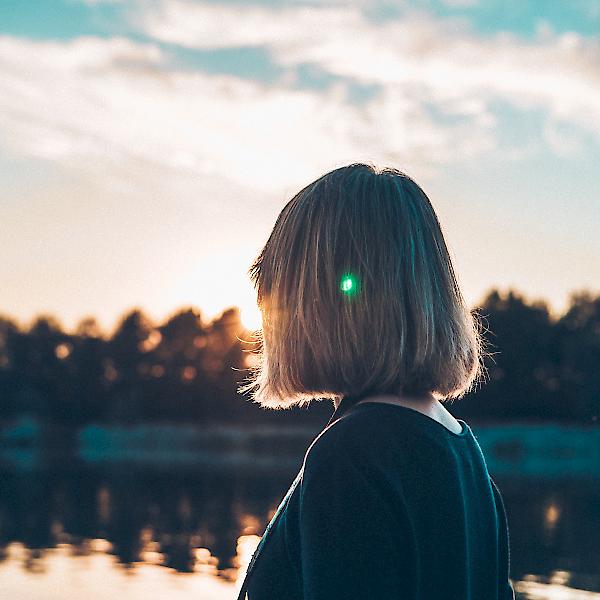 Frau an einem See blickt der Sonne entgegen