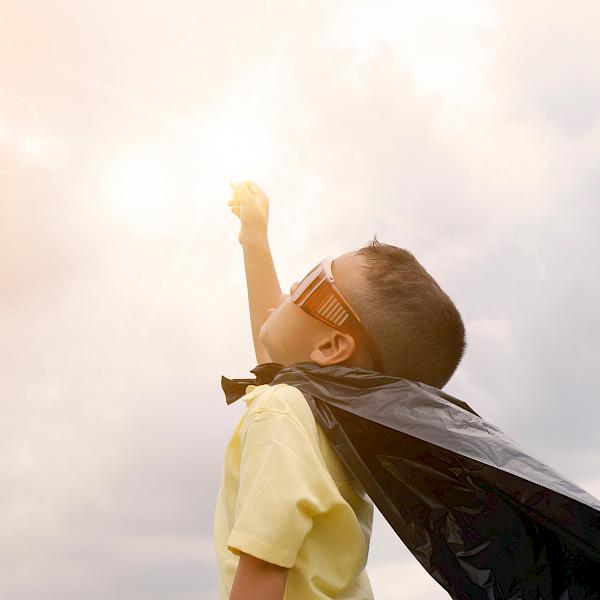 Kleiner Junge im Superhelden-Kostüm streckt die Hand in die Luft