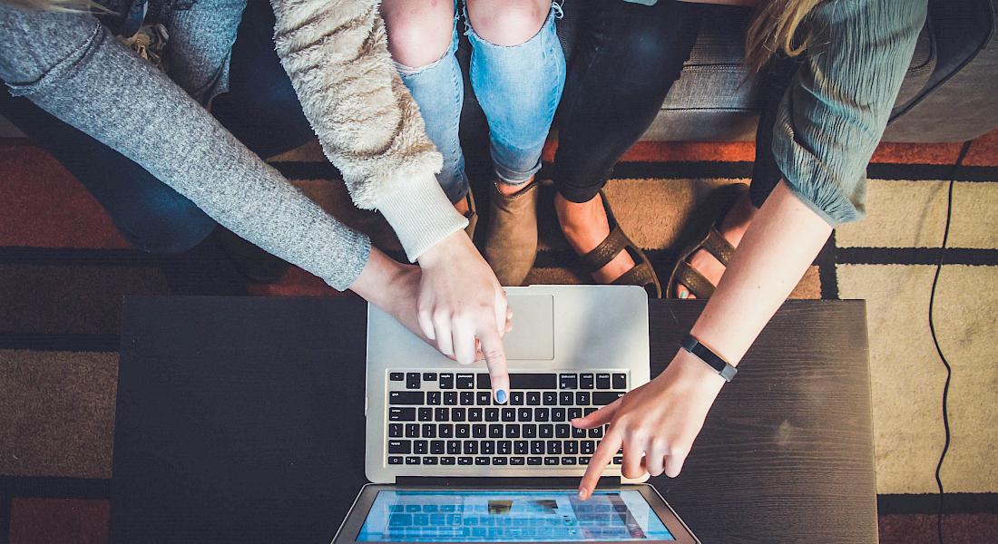 Drei junge Frauen sitzen vor einem Laptop und zeigen darauf