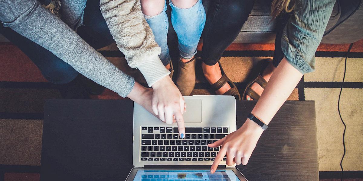 Drei junge Frauen sitzen vor einem Laptop und zeigen darauf