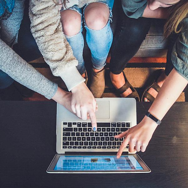 Drei junge Frauen sitzen vor einem Laptop und zeigen darauf