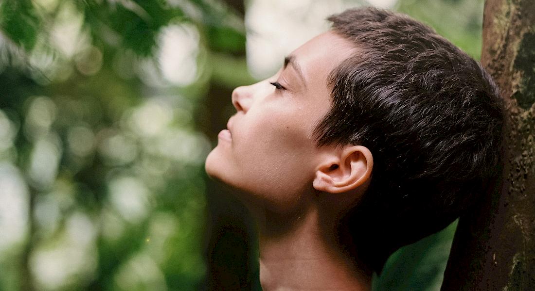 Junge Frau lehnt mit geschlossenen Augen an einem Baum